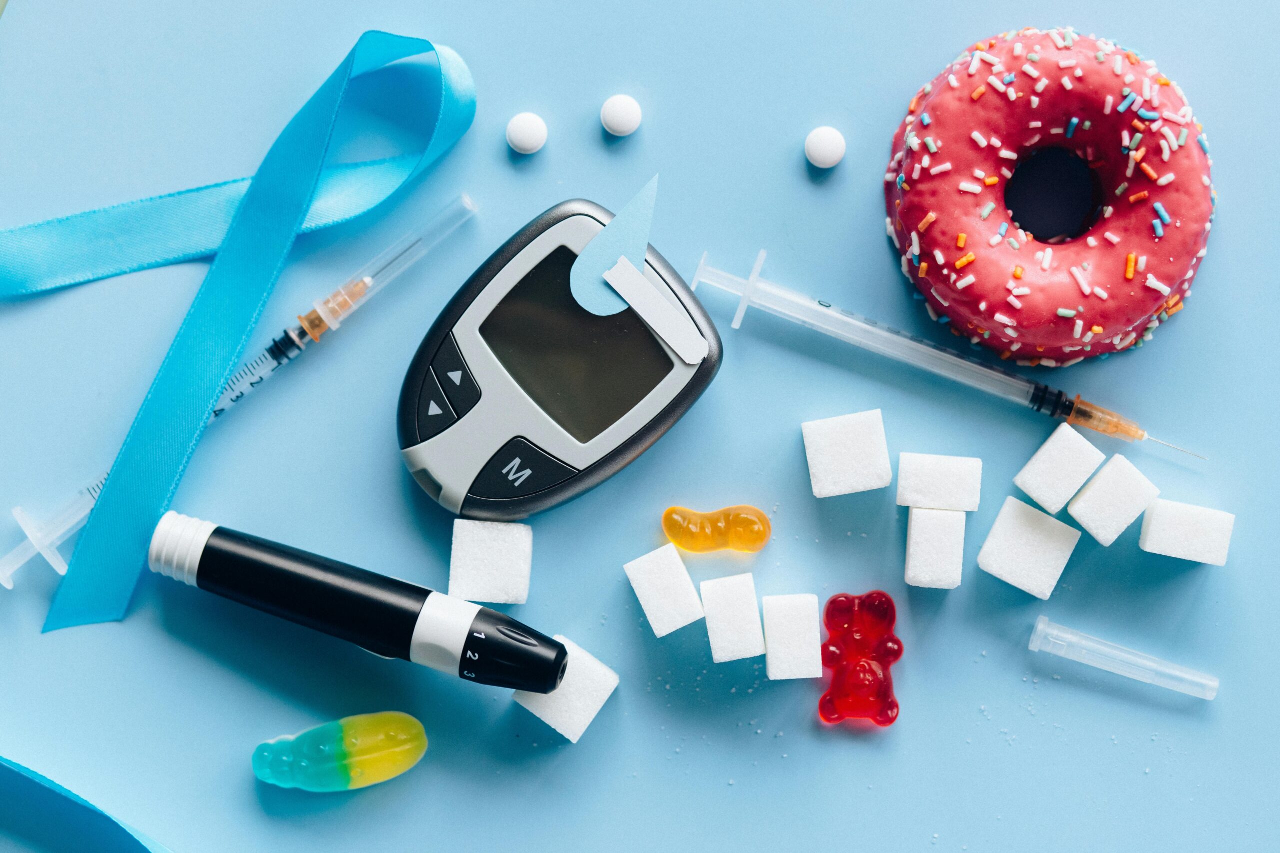 A diabetes management setup with a glucose meter, insulin syringe, sugar cubes, and unhealthy sweets, symbolizing the impact of blood sugar regulation on health.