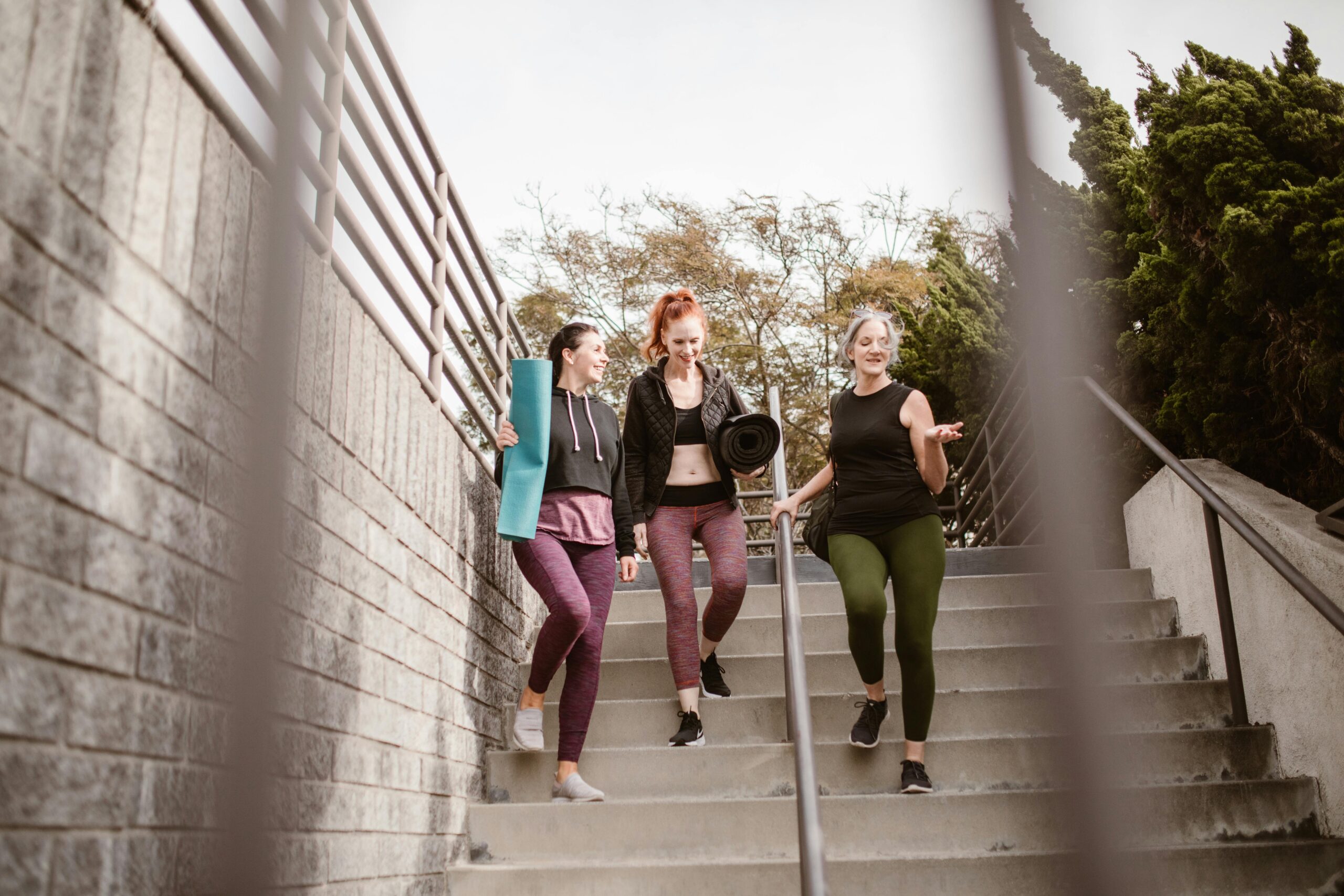 A group of three women walking down outdoor stairs in activewear, enjoying the health benefits of walking for fitness and fat loss.