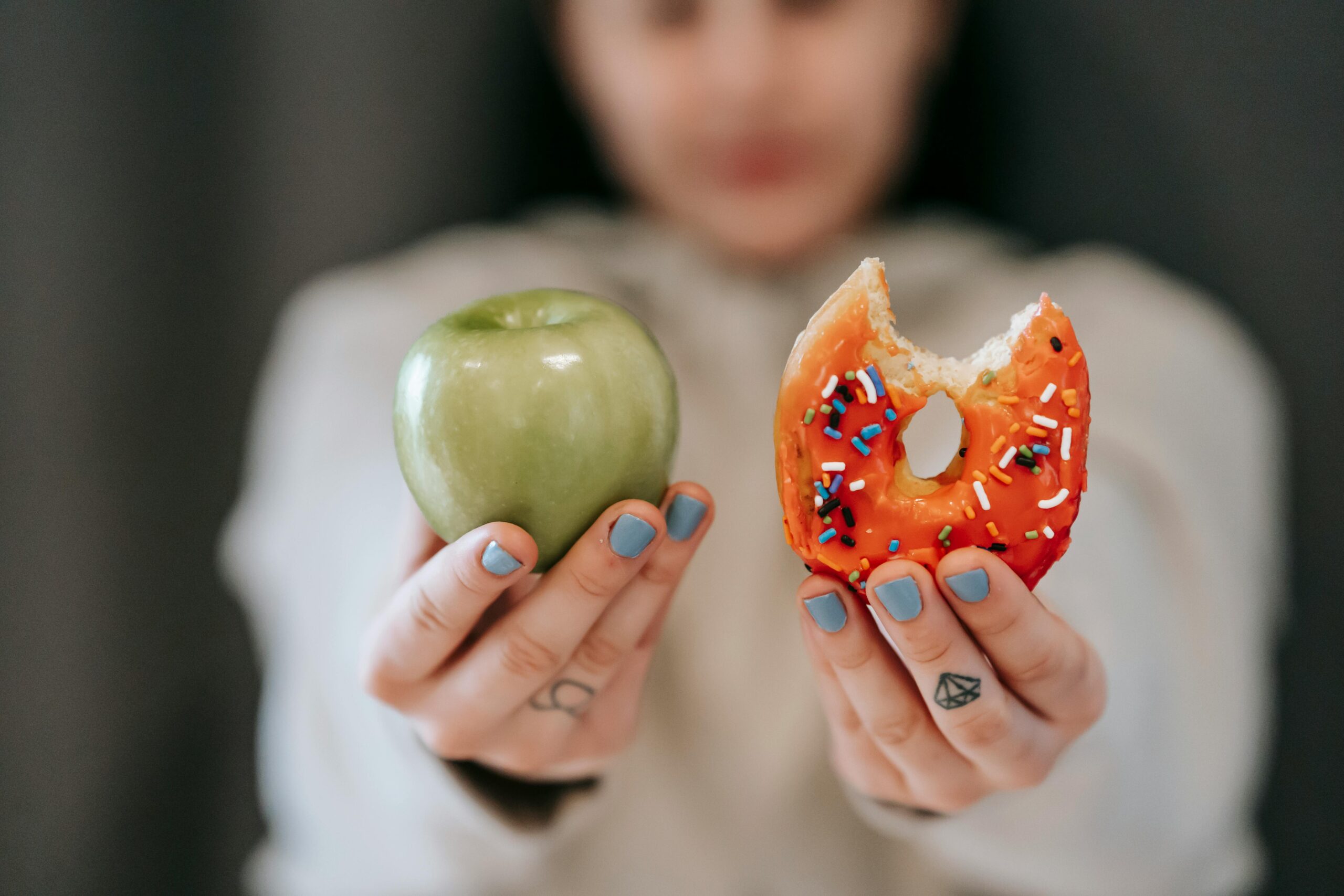 A person holding an apple in one hand and a donut in the other, symbolizing the choice between healthy and unhealthy foods.